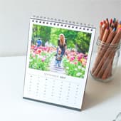 Desk calendar with a spiral binding displaying a colourful photo for September next to a jar of coloured pencils