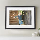 Framed print featuring a child playing in autumn leaves, perfect for home decor